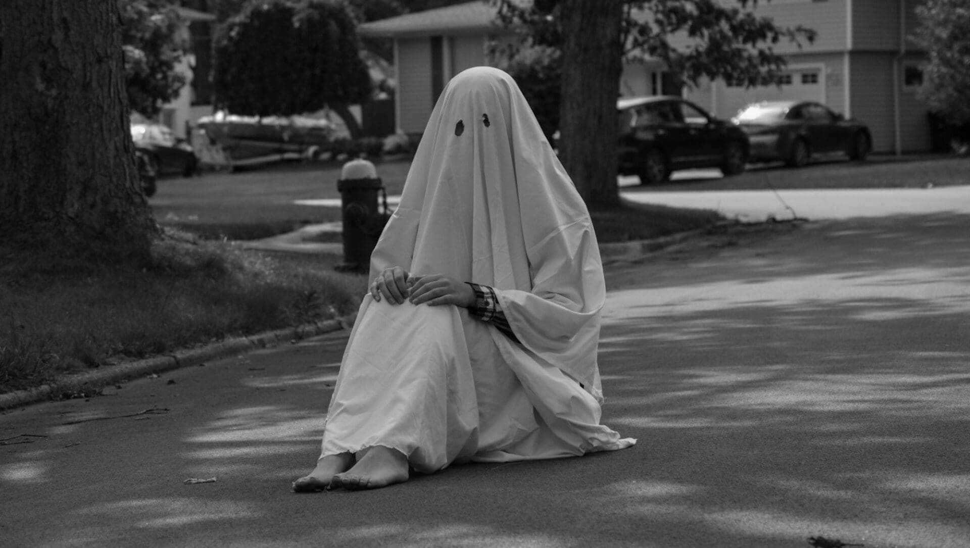 Person dressed as a ghost sitting on a road alone